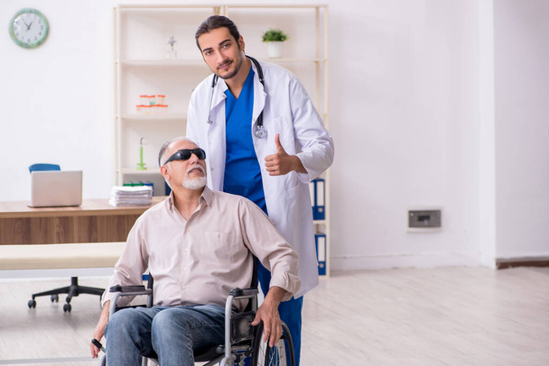 Oude blinde man op bezoek bij jonge mannelijke arts - Foto, afbeelding