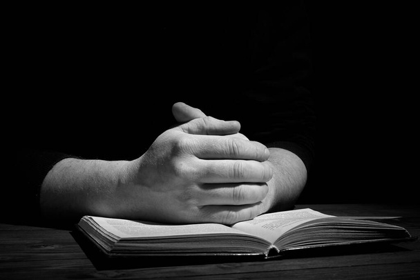 Deux mains sur un livre. Un homme prie dans le noir. La Bible. - Photo, image