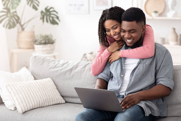 Pareja afroamericana feliz navegando por Internet en el ordenador portátil en casa
 - Foto, imagen