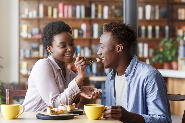 Beautiful black girl feeding yummy pie to her boyfriend at cozy cafe - Foto, Imagen