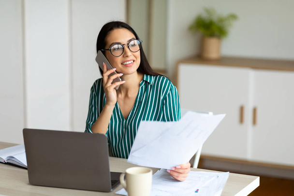 Emprendedora hablando por celular sentada en el lugar de trabajo en la oficina
 - Foto, imagen