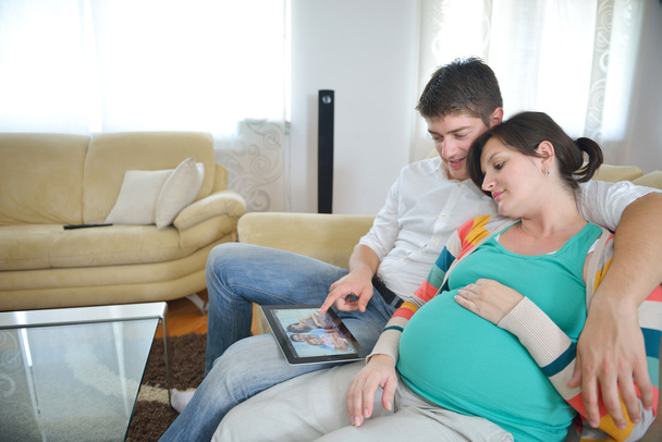 Pregnant couple at home using tablet computer - Fotó, kép