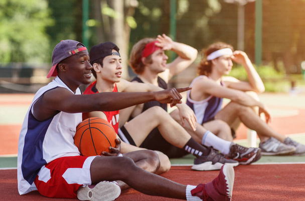 Χιλιετή αθλητές επικοινωνούν κατά τη διάρκεια της ανάπαυσης τους στο γήπεδο μπάσκετ, outdoos. Ελεύθερος χώρος - Φωτογραφία, εικόνα