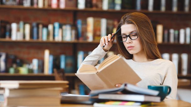 Mladá žena v brýlích čtení knihy sedí v kavárně - Fotografie, Obrázek