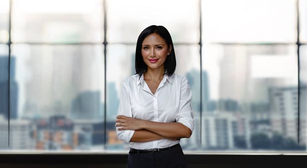 Portrait of a Smiling Mixed Races Business Woman, Crossed Arm and Look into the Camera. Blurred Office Building in the City as background - Fotoğraf, Görsel