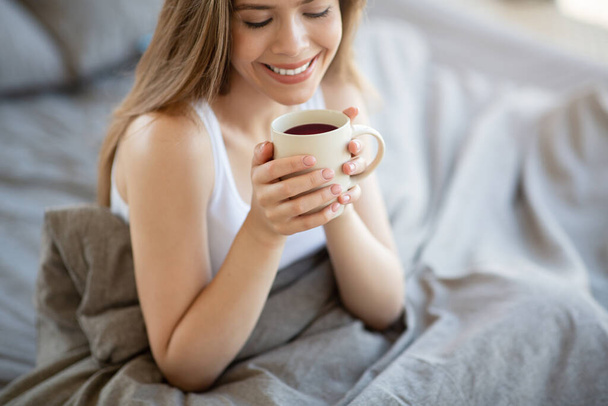 Ragazza sorridente che ha una tazza di caffè fresco sul letto al mattino - Foto, immagini