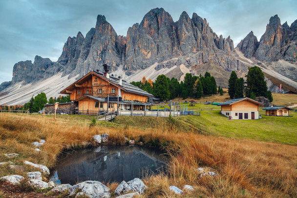 Picturesque autumn alpine landscape, cute wooden chalets and small lake with high mountains in background, Geisler - Odle mountain group, Alto Adige, Dolomites, Italy, Europe - Photo, Image