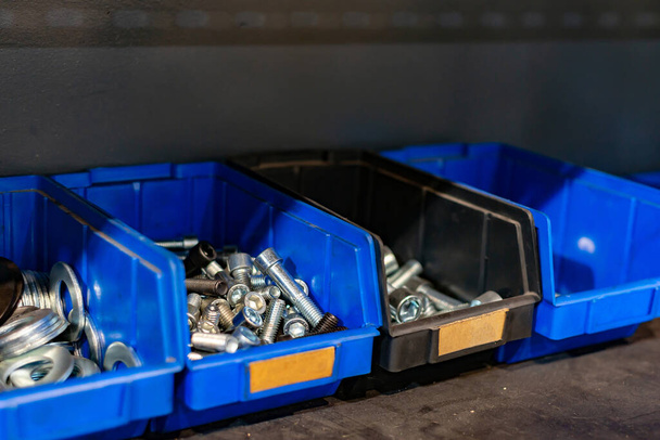 Parafusos de aço galvanizado, parafusos, porcas em uma caixa de plástico azul em um rack em um armazém
. - Foto, Imagem