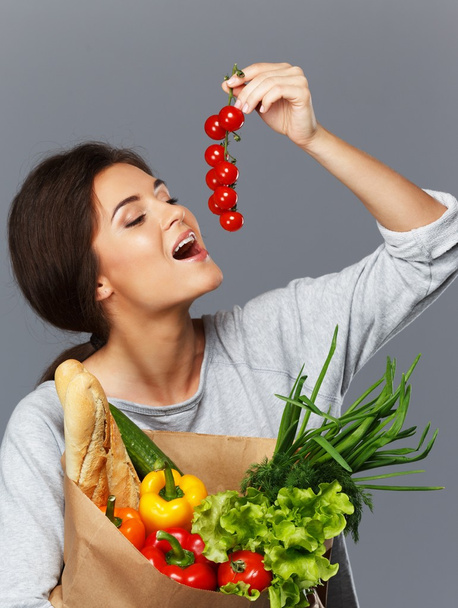 lachende brunette vrouw met kruidenier zak vol met verse groenten en cherry tomaten - Foto, afbeelding