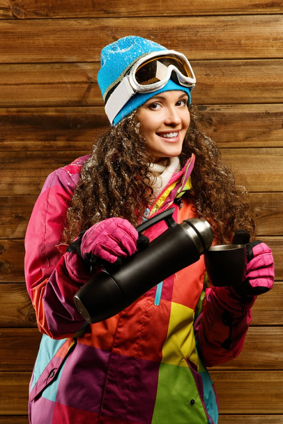 Счастливая женщина в лыжной одежде с термосом против деревянной стены
 - Фото, изображение
