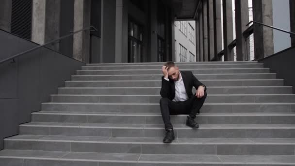 Een ontslagen kantoormedewerker zit op de trap en houdt zijn hoofd in crisis. - Video