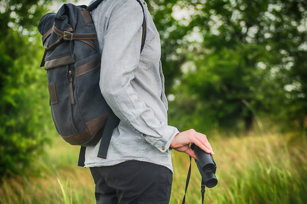 Young adult in shirt with gray backpack holding a binocular for looking around or bird watching. Travel concept - Φωτογραφία, εικόνα