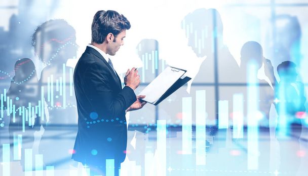 Side view of thoughtful young CEO with clipboard in blurry panoramic Moscow city office with double exposure of digital graphs and diverse business team. Concept of trading and investment. Toned image - Foto, Imagem