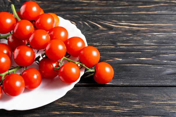 Cherry tomatoes in the white plate on the dark wooden table. Juicy ripe vegetables on a black background. Healthy eating. vegetarian food - Foto, afbeelding