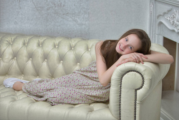 Beautiful young girl sitting on the sofa by the fireplace. - 写真・画像