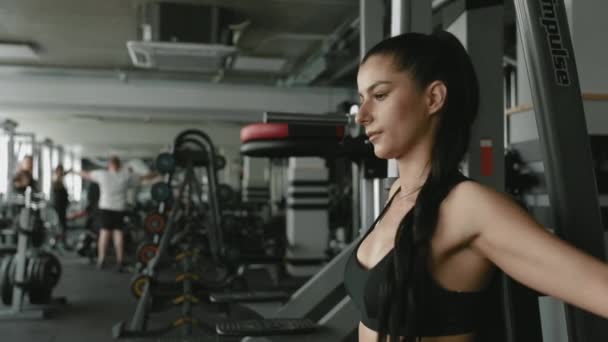 Confident fitness girl with dark hair in sportswear using gym simulator for pumping muscles on during regular workout. Concept of strength, self discipline and healthy lifestyle. - Materiaali, video