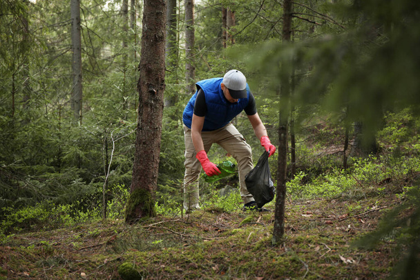 Man cleans garbage and plastic bottle in forest. Green volunteering. Caring for environment. - Foto, imagen