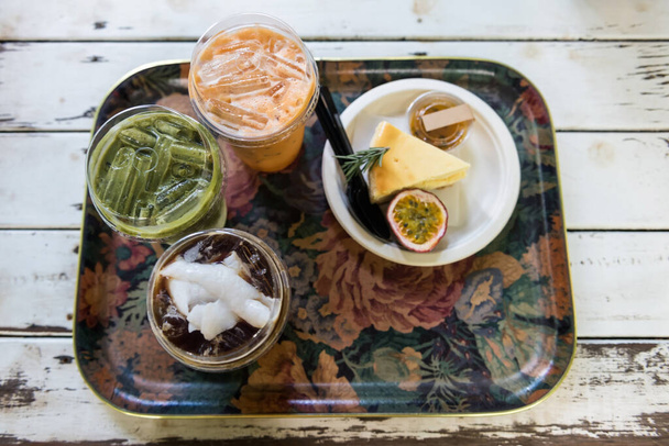 Americano kawa lodowa z kokosem, japoński matcha zielona herbata, czerwona herbata tajska, i sernik z marakuji owoców na białym drewnianym stole przez widok z góry w kawiarni. Niezdrowe jedzenie słodkiej pustyni. - Zdjęcie, obraz