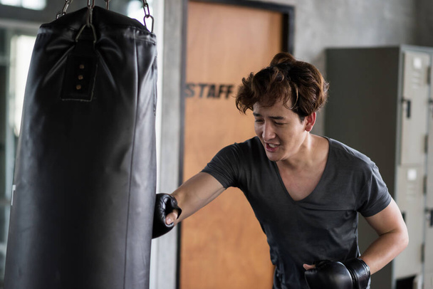 Genç Tayland asıllı Amerikalı jimnastik salonunda boks kum torbasını yumrukluyor. Sağ el sertçe vuruyor. Muay Thai egzersizi ya da egzersiz. Vücut geliştirme ve sağlıklı yaşam tarzı konsepti. - Fotoğraf, Görsel