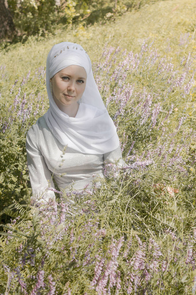 young muslim woman sit on the ground among the plants. Summer field. - Φωτογραφία, εικόνα