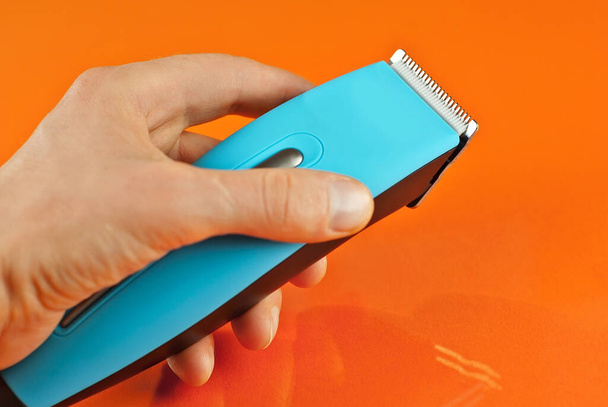 Hair clipper in hand close up. Blue hairdresser tool on orange background. Layout for design. - Zdjęcie, obraz