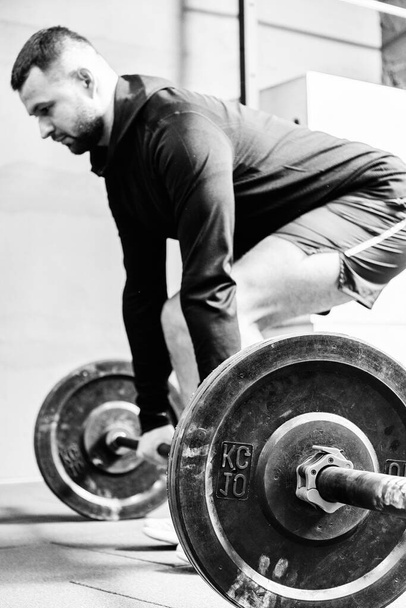Spor kıyafetli genç bir adam spor salonunda antrenman yaparken ağırlık kaldırmaya hazırlanıyor. Fitness sporu veya sağlıklı yaşam tarzı konsepti. - Fotoğraf, Görsel