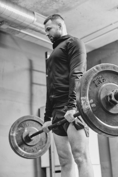 Fit junger Mann in Sportbekleidung bereitet sich während einer Trainingseinheit in einem Fitnessstudio darauf vor, Gewichte zu heben. Fitnesssport oder gesundes Lebensstil-Konzept. - Foto, Bild