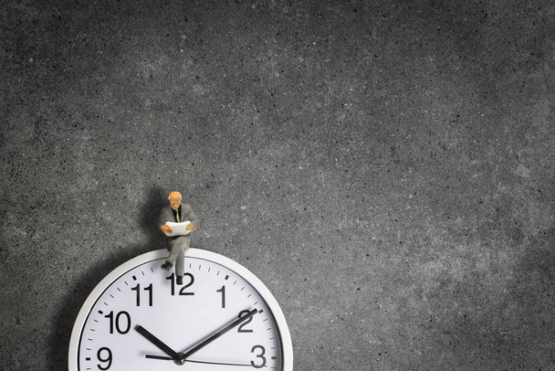 Time Management Concept: Miniatyyri liikemiehenä istua seinäkellon päällä ja lukea sanomalehteä. - Valokuva, kuva