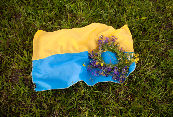 Bandeira nacional amarelo-azul da Ucrânia e uma grinalda de flores silvestres em um fundo de grama verde. Dia da Independência da Ucrânia. Dia Nacional da Bandeira da Ucrânia. Dia da Constituição. símbolo
 - Foto, Imagem