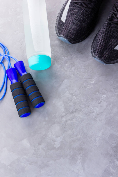 Fitness concept with sneakers, jump rope and bottle of water. Sports equipment on a gray background. Healthy lifestyle concept. Copy space. Top view - Photo, Image