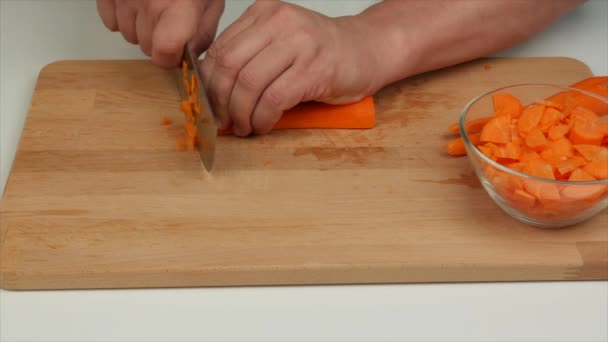 Man cuts carrots with a cook knife on a wooden board, closeup - healthy diet food - Footage, Video