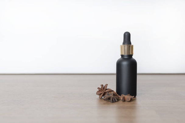 black Cosmetic bottle with pipette near star anise on white and wooden background. - Foto, Imagen