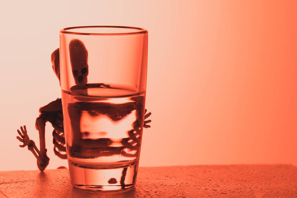 a skeleton peeps out from behind a glass of alcohol. poison in a pile - Photo, image