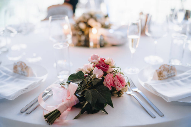 Brautstrauß aus rosa Rosen, Eustoma, Hedera und rosa Schleifen auf dem Hochzeitstisch - Foto, Bild