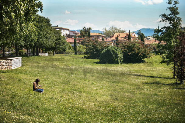 solitary woman sitting on grass, she's using smartphone - Photo, Image