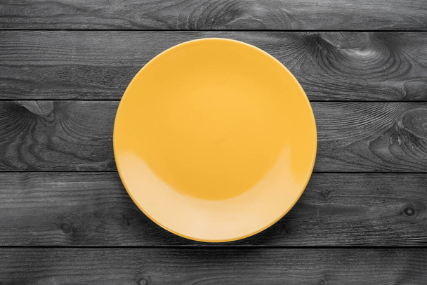 Empty yellow plate on textured black wooden table. Top view - Foto, immagini