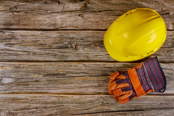 Guantes de trabajo de cuero amarillo casco de seguridad desgaste duro en el sitio de construcción en un fondo de madera
 - Foto, Imagen