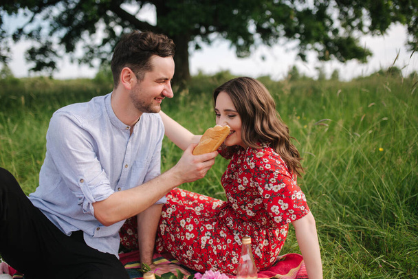 Mutlu erkek ve kadın çifti kırmızı battaniyeye oturur. Kadın ekmeği. - Fotoğraf, Görsel