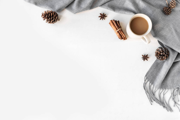 Autumn or winter cozy composition with gray warm blanket and cup of coffee. Seasonal autumnal coziness with soft plaid, coffee, cinnamon and cones. Cozy home and hygge concept on white background, copy space. - Фото, зображення