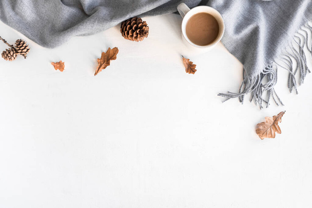 Autumn cozy composition with gray warm blanket and cup of coffee. Seasonal autumnal coziness with soft plaid, coffee, leaves and cones. Cozy home and hygge concept on white background, copy space. - Photo, Image