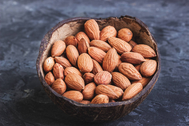 Almonds in coconut shells on a dark background - Photo, image