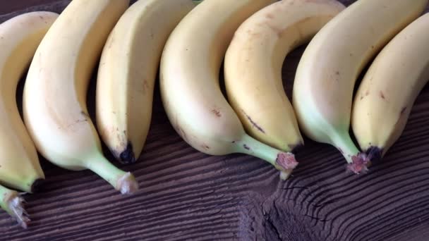 Banane mature gialle si trovano in fila su una superficie del tavolo vintage in legno - Filmati, video