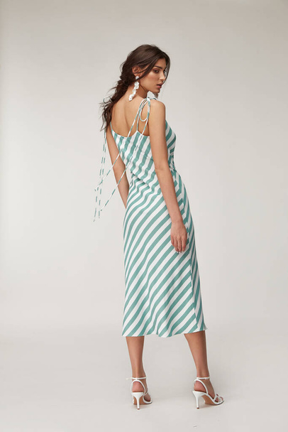 Fashion pretty woman beautiful makeup perfect body shape tanned skin wear clothes summer collection organic textile blue stripes silk dress stylish sandals shoes, accessory jewelry earrings romantic. - Foto, Imagen