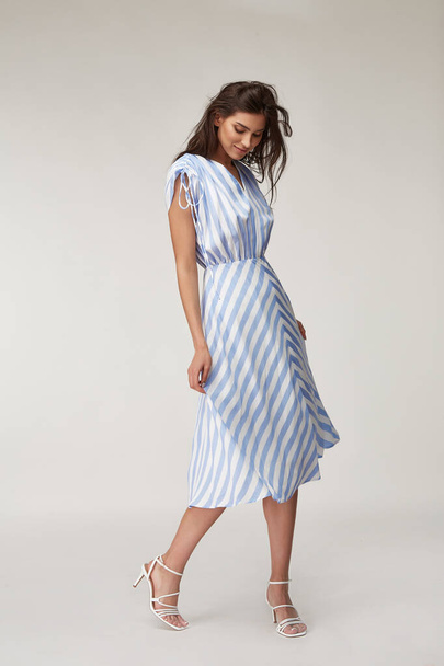Sexy fashion model beautiful woman pretty face natural makeup, tanned skin body  wear summer collection clothes style for romantic date walk casual trendy light silk in white blue stripes long dress. - 写真・画像