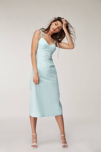 Woman beautiful face natural make up brunette hair tanned skin body wear fashion summer collection organic cotton long light blue skinny dress style for romantic date walk, accessory shoes sandals. - 写真・画像