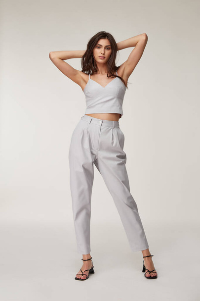 Fashion pretty woman beautiful makeup perfect body shape tanned skin wear clothes summer collection organic textile cotton light gray suit crop top and trousers stylish sandals shoes. - Valokuva, kuva