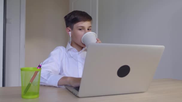 Bonito menino jovem empresário trabalhar em um laptop em casa e beber café. Aprendizagem online, lição à distância, educação em casa. Criança usando computador portátil
. - Filmagem, Vídeo