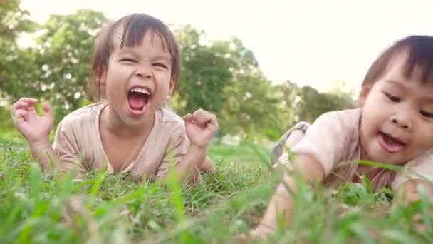 Két boldog testvér lány fekszik a zöld füvön a nyári parkban.. - Felvétel, videó