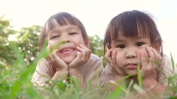 Dvě šťastné sourozenecké dívky ležící na zelené trávě venku v letním parku. - Záběry, video