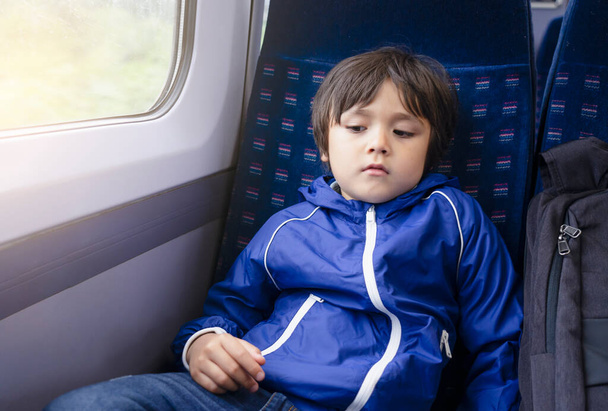 Portrét malého chlapce s znuděným obličejem, jak sedí sám ve vlaku, školka cestuje vlakem, dítě s nešťastnou tváří, které není šťastné, že se vrací do školy, rozmazlený dětský koncept - Fotografie, Obrázek